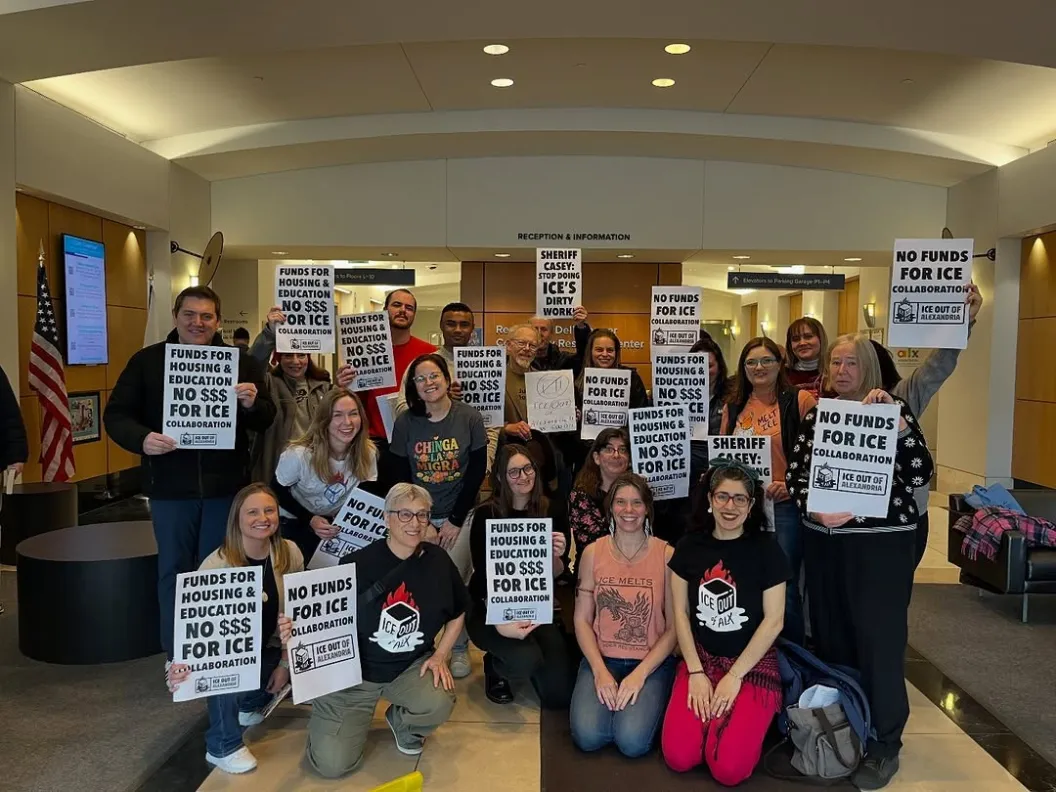 about 20 people standing and sitting together holding signs encouraging defunding collaboration with ICE